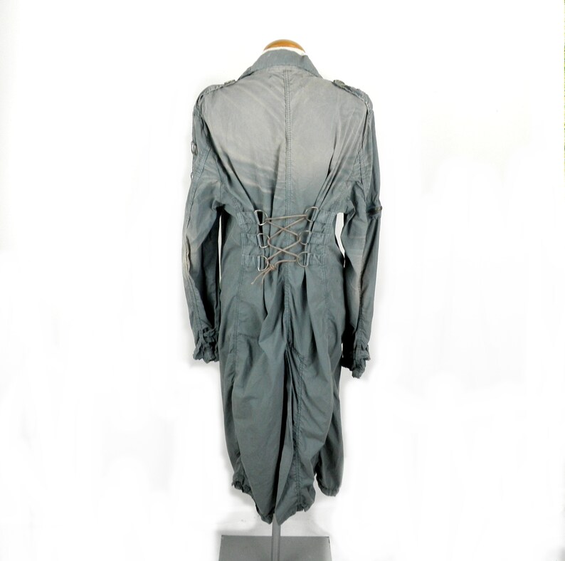 May include: A long, gray, cotton jacket with a lace-up back detail. The jacket has a collar and long sleeves.