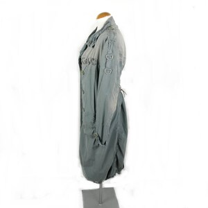 May include: A long, gray,  cotton jacket with a  ruched detail on the front and a  lace-up back. The jacket has a  button closure and  two large metal rings on the sleeves.