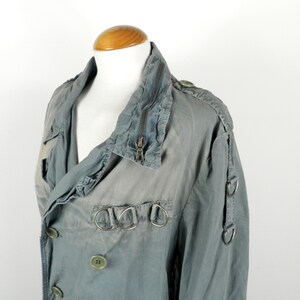 May include: A gray, double-breasted jacket with a zipper closure and multiple silver rings on the front and sleeves.