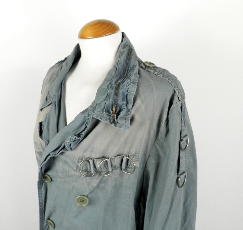 May include: A gray, double-breasted jacket with a zipper closure and multiple silver rings on the front and sleeves.