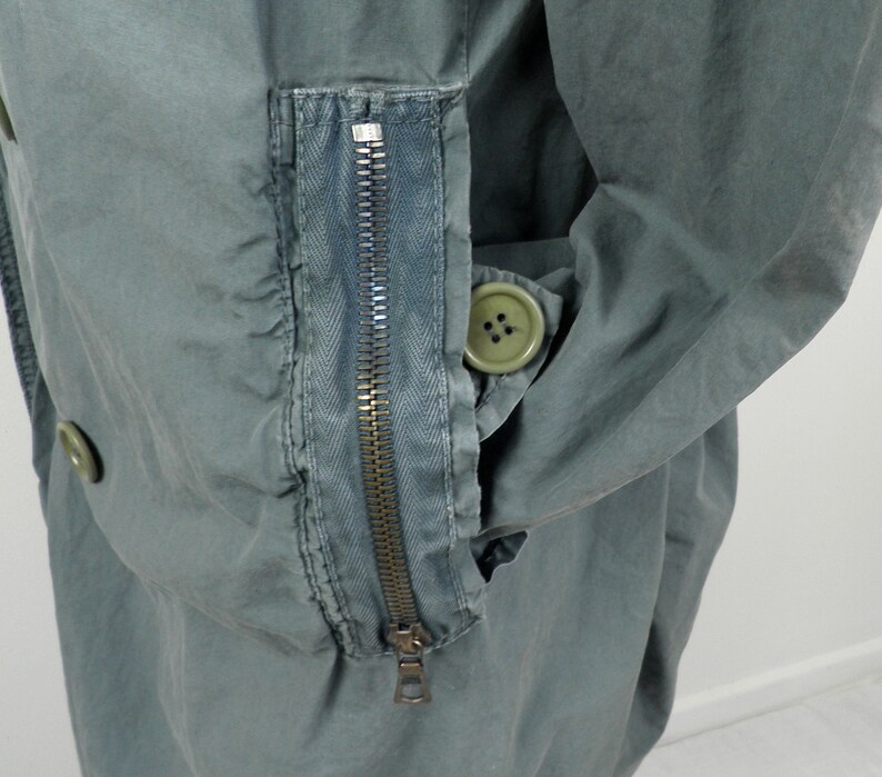 May include: A green utility jacket with a zippered pocket on the sleeve and a button closure. The jacket has a relaxed fit and a casual style.