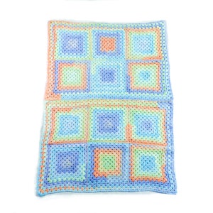 May include: A handmade, colorful crochet blanket featuring a square pattern in shades of blue, green, orange, and peach. The blanket is made of soft yarn and is perfect for a baby or as a decorative throw.