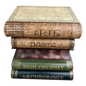 May include: A stack of decorative books with titles including "ARTS", "DANTE", "PHILOSOPHY", and "ARCHEOLOGY". The books have a vintage aesthetic, with aged-looking covers in shades of beige, brown, green, and navy blue. The titles are in gold lettering.