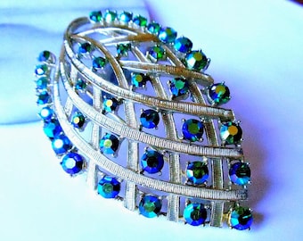 Könnte beinhalten: Eine Vintage-Brosche in Silberoptik mit Blattdesign, verziert mit irisierenden blauen und grünen Strasssteinen. Die Brosche hat eine gitterartige Struktur mit mehreren runden und quadratischen Steinen, die einen funkelnden Effekt erzeugen.
