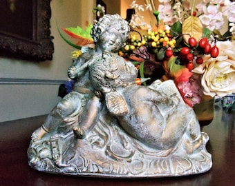 May include: A pair of cherubs sculpted in a distressed gold and green finish. The cherubs are sitting on a decorative base with intricate details.