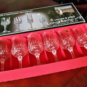May include: A set of six lead crystal stemglasses in a red box. The glasses have a diamond-cut pattern and are labeled as "Longchamp n°2". The box also displays the text "6 25 cl lead Crystal stemglasses".