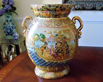 May include: A large, ornate ceramic vase with a wide mouth and two gold handles. The vase features a detailed, colorful scene of figures on a boat, with gold accents and floral patterns. The vase is a decorative piece.