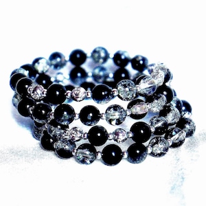 May include: A multi-strand wrap bracelet featuring alternating smooth black spherical beads and textured, translucent gray crackle-effect beads. Small silver-toned metallic spacer beads are positioned between the larger spherical beads throughout the design.