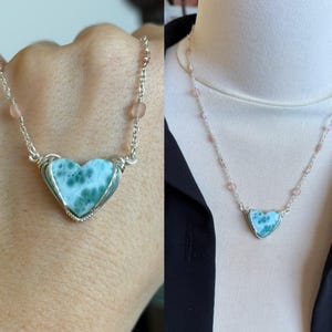 May include: A silver necklace with a heart-shaped larimar stone pendant. The pendant is wire-wrapped and has a light blue colour with white marbling. The necklace includes pink beads and a delicate chain.