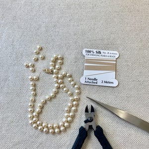 May include: A strand of white pearls with a gold clasp, a spool of 100% silk thread for stringing pearls and beads measuring 2 meters with one needle attached, and a pair of black-handled wire cutters with a sharp metal tip for jewelry making.