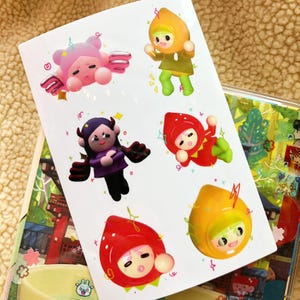 Puede incluir: Una hoja de pegatinas coloridas con personajes de dibujos animados con disfraces de temática frutal. Los personajes son un hada rosa, un diablo morado, una fresa roja, un limón amarillo y una manzana verde. Las pegatinas son perfectas para agregar un toque de fantasía a los diarios, las computadoras portátiles o las botellas de agua.