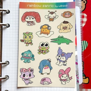 May include: A sheet of colorful stickers featuring various cartoon characters. The stickers include a variety of animals and creatures, such as a bunny, bee, monkey, frog, and penguin. The text "rainbow sanrio by w0nkko" is printed at the top.