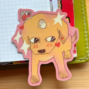 May include: A sticker featuring a cartoon dog with a light brown coat and large eyes. The dog is surrounded by pink accents, including stars and hearts. The word "home" is in a red box at the top.