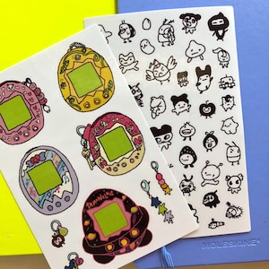 May include: Two sheets of stickers. One sheet features five colorful Tamagotchi-style digital pet toys. The other sheet features a variety of black and white cartoon characters, including frogs, birds, and a robot.