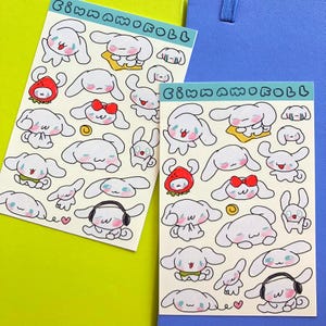 May include: Two sheets of stickers featuring a cartoon dog with different expressions. The dog is white with blue eyes and pink cheeks. The stickers are on a yellow and blue background. The text "Cinnamoroll" is printed on each sheet.
