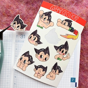 May include: A set of nine Astro Boy stickers featuring different expressions and poses. The stickers are drawn in black and white with some color accents. The stickers are on a white background with the word "ASTROBOY" written in red at the top.