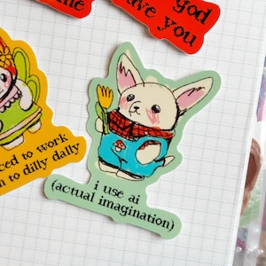 May include: A collection of colorful stickers on a grid-lined surface. One sticker features a cartoon rabbit in blue overalls and a red scarf, holding a yellow flower. Text on the sticker reads "i use ai (actual imagination)." Other stickers have text.