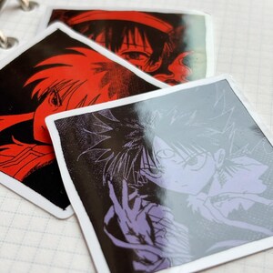 Puede incluir: Pegatinas cuadradas con ilustraciones de estilo anime. Una tiene un dise&ntilde;o rojo y negro, otra una imagen morada y negra. Las pegatinas tienen bordes blancos y est&aacute;n sobre una p&aacute;gina de cuaderno.