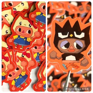 May include: A collection of orange die-cut stickers featuring cartoon characters. One design shows a character in a cat-like hat and overalls. Another sticker shows a character with a black crown and a determined expression. The stickers have a red border.