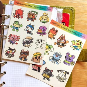 Puede incluir: Dos hojas de pegatinas con ilustraciones coloridas de personajes de Animal Crossing. Las pegatinas tienen un borde de arcoíris y el texto "rainbow animal crossing by wønkkø". Las pegatinas están sobre un fondo blanco.