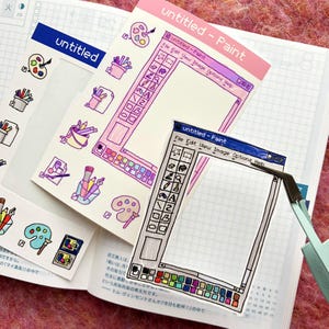 Op de afbeelding: Een verzameling stickers met een handgetekend kunstthema. De stickers hebben een roze en blauw kleurenschema, met de tekst "untitled - Paint" en illustraties van verfpaletten, penselen en een computerverfprogrammavenster.
