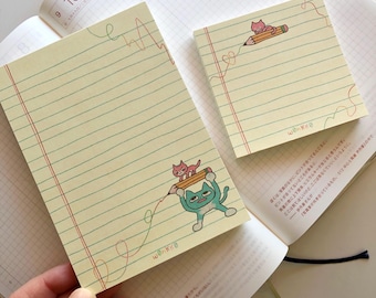 May include: Two yellow lined memo pads with a cat and pencil illustration. The text "ωθηκέθ" is printed on the bottom of each pad.