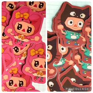 May include: A collection of pink and brown character stickers. The pink stickers feature a character in a pink outfit with a bow. The brown stickers depict a character in a cat costume. The stickers are cut out and ready to use.