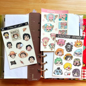May include: A collection of colorful stickers featuring characters from the anime series One Piece. The stickers include images of Luffy, Chopper, and other characters. The stickers are displayed in a planner with a brown ruler and the text "STRAW HAT LUFFY", "WANTED", and "PIRATE PALS!"