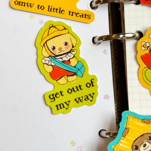 May include: A sticker featuring a cartoon puppy wearing a yellow hat and red outfit, with the text "get out of my way." Another sticker above reads "omw to little treats."