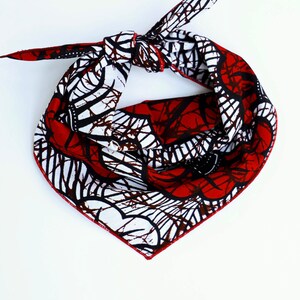 May include: A red, white, and black bandana with a geometric pattern. The bandana is tied in a knot and is ready to be worn.