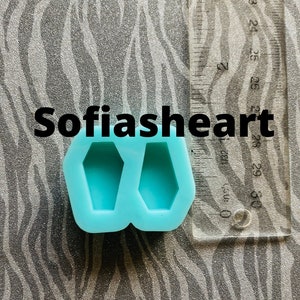 May include: A blue silicone mold with two coffin-shaped cavities. The mold is approximately 2.5 inches wide and 1.5 inches tall. The mold is on a gray and white patterned surface. The text "Sofiasheart" is visible in the image.