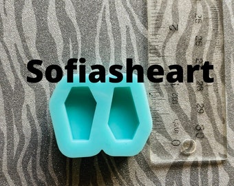 May include: A blue silicone mold with two coffin-shaped cavities. The mold is approximately 2.5 inches wide and 1.5 inches tall. The mold is on a gray and white patterned surface. The text "Sofiasheart" is visible in the image.