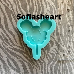 May include: A light blue silicone mold shaped like a Mickey Mouse head with a lollipop stick attached. The mold is for making candy or other treats.