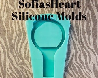 May include: A turquoise silicone mold for making a ring with a round center and a small handle. The mold is about 2 inches in diameter and is shown next to a ruler.
