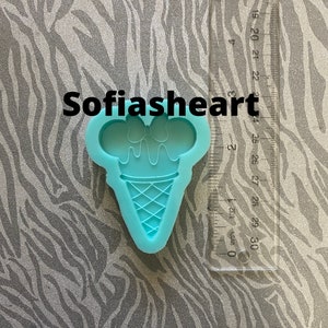 May include: A light blue silicone mold shaped like an ice cream cone with a bow on top. The mold is on a zebra patterned surface.