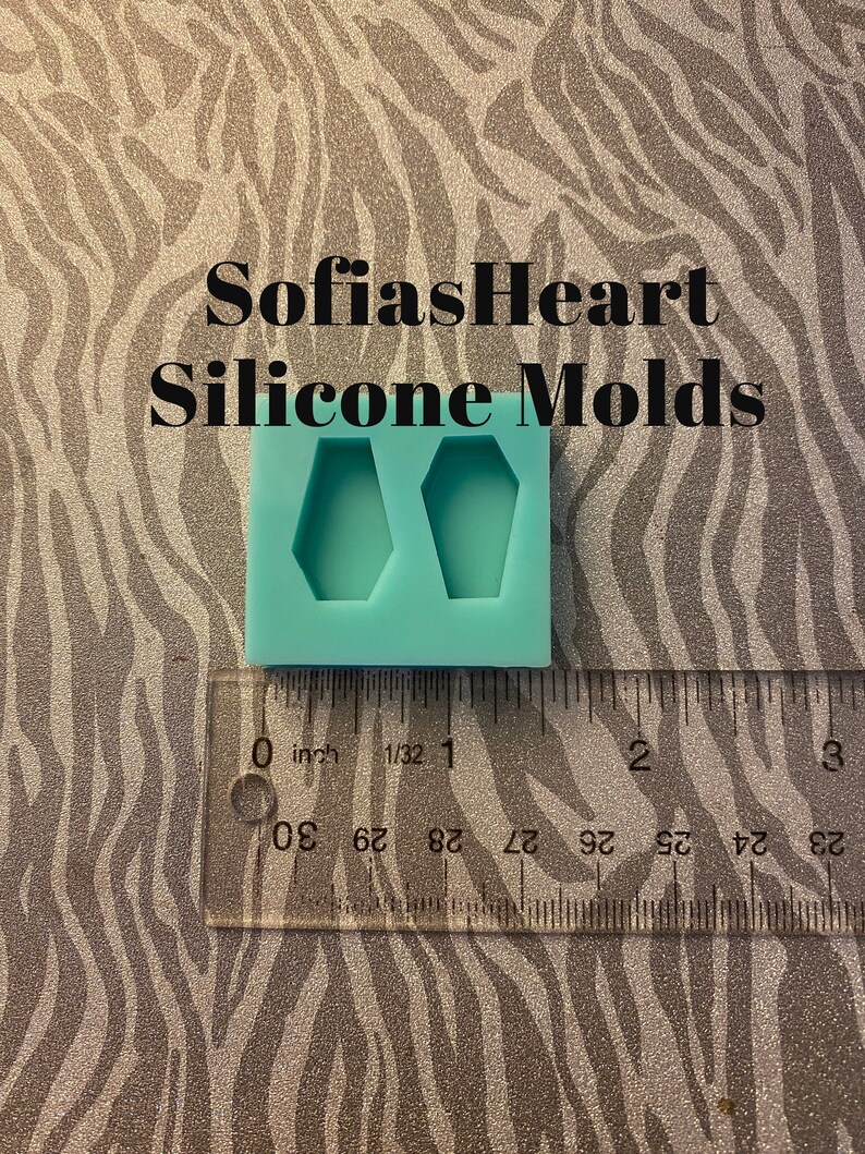 May include: A turquoise silicone mold with two coffin-shaped cavities. The mold is approximately 1 inch wide and is shown next to a ruler.