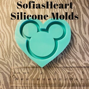 Puede incluir: Un molde de silicona azul claro en forma de corazón con orejas de Mickey Mouse. El molde mide aproximadamente 5 cm de ancho.