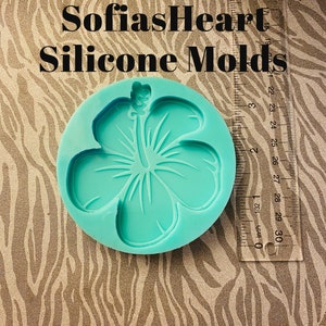 Puede incluir: Un molde de silicona azul turquesa con forma de flor de hibisco. El molde está sobre un fondo de estampado de cebra marrón y blanco. SofiasHeart Silicone Molds está escrito en negro sobre el molde.