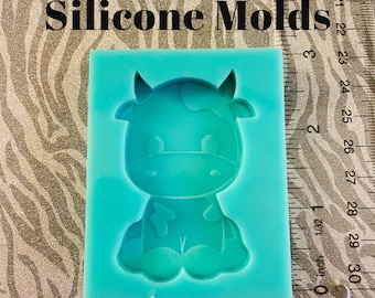 May include: A light blue silicone mould shaped like a cartoon cow with black spots. The mould is approximately 5 cm tall and 4 cm wide. The text "SofiasHeart Silicone Molds" is visible above the mould.