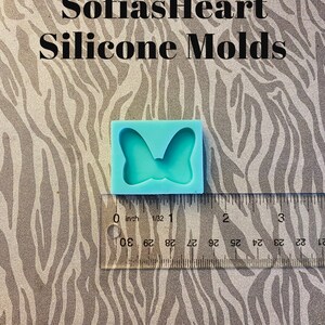 Puede incluir: Un molde de silicona azul claro con forma de lazo. El molde mide aproximadamente 2,5 cm de ancho y est&aacute; sobre una regla.