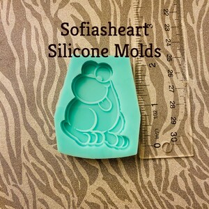 May include: A light blue silicone mold shaped like a cartoon frog with big eyes and a wide smile. The mold is sitting on a brown and white zebra print background. The text "Sofiasheart Silicone Molds" is visible above the mold.
