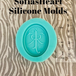 May include: A turquoise silicone mold with a raised design of a stylized symbol. The symbol is a stylized letter "T" with a small circle at the top and bottom. The mold is on a zebra print background.