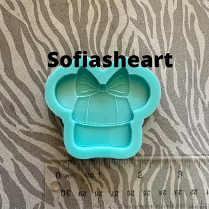 May include: A turquoise blue silicone mold shaped like a cartoon character wearing a hat with a bow. The mold is approximately 1 inch in diameter.