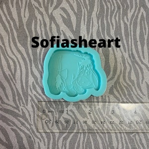 May include: A light blue silicone mold featuring a cartoon donkey character with a bow. The mold is placed on a silver and gray zebra-striped surface. The text "Sofiasheart" is above the mold.