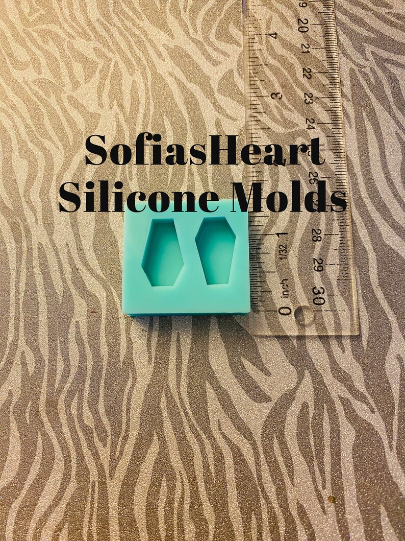 May include: A blue silicone mold with two coffin-shaped cavities. The mold is on a zebra-print surface with a ruler in the background. The text "SofiasHeart Silicone Molds" is visible in the image.