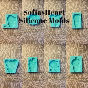 May include: Set of seven silicone molds featuring various cartoon characters. The molds are light blue and are displayed on a zebra-striped surface. The molds are approximately 2 inches in size.