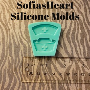 May include: A teal blue silicone mold shaped like a nurse's hat with a red cross on the top and bottom. The mold is approximately 1 inch in size.