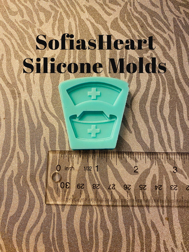 May include: A teal blue silicone mold shaped like a nurse's hat with a red cross on the top and bottom. The mold is approximately 1 inch in size.