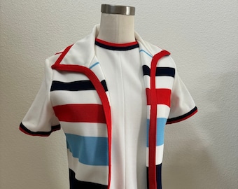 May include: A white dress with a striped, short-sleeved top. The top has red, blue, and black stripes with a white background. The dress has a collar and a short sleeve.