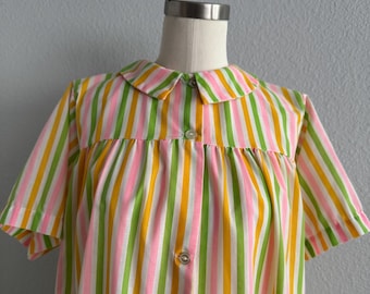 Op de afbeelding: Een jurk met korte mouwen, een Peter Pan-kraag en knoopsluiting. De jurk heeft verticale strepen in roze, groen en geel. Het kledingstuk wordt op een mannequin gepresentteerd tegen een grijze achtergrond.